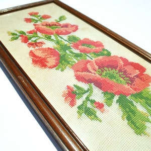 May include: A framed cross-stitch embroidery featuring a bouquet of red poppies with green leaves and stems on a white background.
