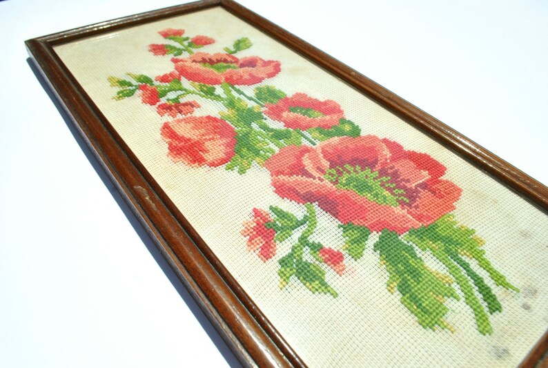 May include: A framed cross-stitch embroidery featuring a bouquet of red poppies with green leaves and stems on a white background.