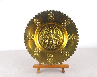May include: A gold metal decorative plate with a scalloped edge and a raised floral design in the center. The plate is on a small wooden easel.
