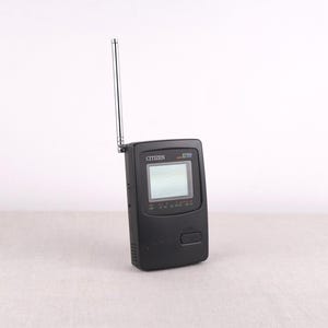Könnte beinhalten: Ein schwarzes tragbares Citizen-Fernsehgerät mit einer nach oben ausgerichteten silbernen Antenne. Der Bildschirm ist sichtbar, und das Gerät hat unten eine Taste. Die Modellnummer ist oben rechts sichtbar.