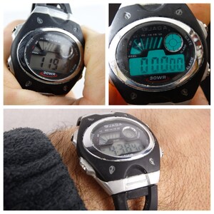 May include: A black and silver digital wristwatch with a black band. The watch face has a digital display showing the time, date, and day of the week. The watch also has a light feature and is water resistant to 30 meters.