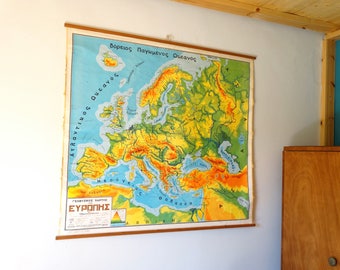 May include: A vintage map of Europe with a wooden frame. The map is in shades of green, yellow, and blue, with the text "Βόρειος Παγωμένος Ωκεανός" at the top. The map is titled "Γεωγραφικός Χάρτης της ΕΥΡΩΠΗΣ".
