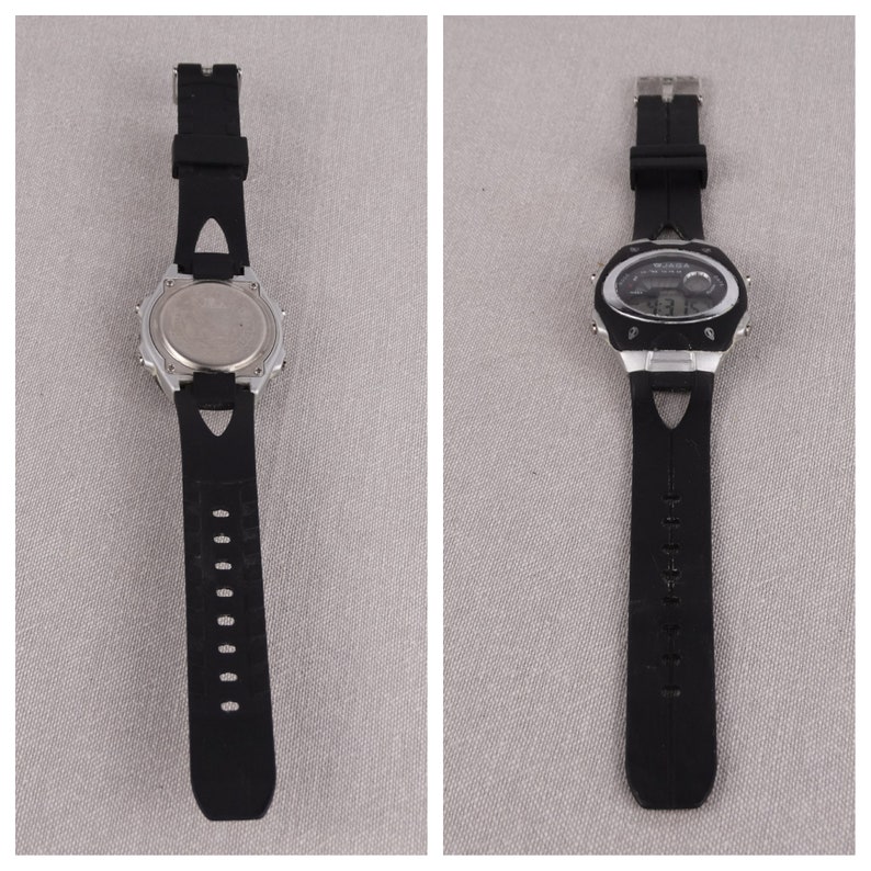 May include: A black digital wristwatch with a silver case and black rubber band. The watch has a digital display with multiple time zones and a stopwatch function.