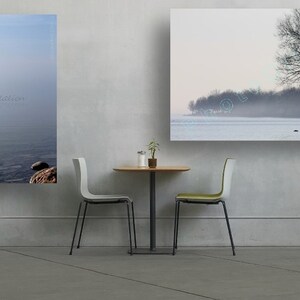 May include: Two framed landscape photographs of a lake with a tree in the foreground and a misty background. The photographs are hanging on a white wall above a small table with two chairs.