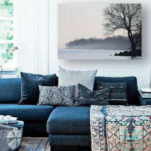May include: A blue sectional sofa with a variety of patterned throw pillows and a throw blanket. The sofa is in front of a wall with a framed print of a foggy lake and a tree.