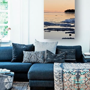 May include: A scenic photograph of a frozen lake at sunset. The water is a deep blue, and the ice is a light blue. The sky is a soft orange and pink. There are trees in the distance.
