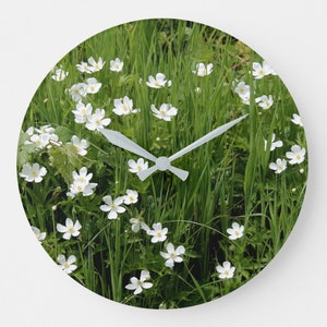 May include: A white clock face with white hands set against a background of green grass and white flowers.