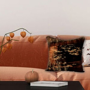 May include: A burnt orange sofa with three throw pillows. The pillows have black and gold geometric patterns, a white and brown geometric pattern, and a solid burnt orange color. A vase with dried branches and a small pumpkin are on the coffee table in front of the sofa.