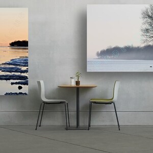 May include: Three framed landscape photographs of a frozen lake with a shoreline of trees in the distance. The photographs are hanging on a white wall above a small table with two chairs.