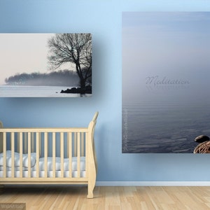 May include: Two framed photographs of a misty lake scene with a tree in the foreground. The top photo has the word "Meditation" written in cursive on the water. The bottom photo shows a tree line in the distance. Both photos are hanging on a light blue wall with a white crib in the foreground.