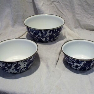 May include: Three white enamel bowls with a blue and white speckled pattern. The bowls are nested inside each other, with the largest bowl on the bottom and the smallest bowl on top.