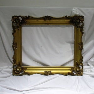 May include: A large, ornate, gold-colored picture frame with a decorative, carved design. The frame is made of wood and has a slightly distressed finish.