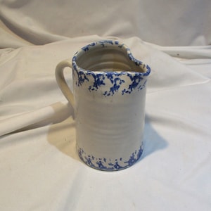 May include: A white ceramic pitcher with a blue and white speckled glaze. The pitcher has a handle and a wide mouth.