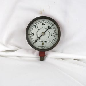 May include: An antique steam pressure gauge with a white face and black numerals. The gauge reads up to 30 PSI and features the text "Pierce, Butler & Pierce Mfg. Corp." and "Steam". The gauge has a red base and a dark metal casing.