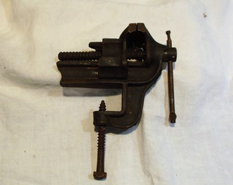 May include: A vintage cast iron bench vise with a threaded screw and a handle. The vise is in good condition with some rust and wear.