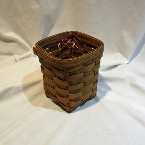 May include: A square, brown wicker basket with a pink ribbon tied around the top.