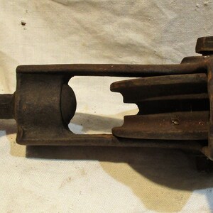 May include: A rusty metal pulley with a single wheel and a handle. The pulley has a metal loop on the side for attaching a rope.