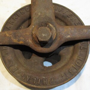 May include: A rusty cast iron pulley with a handle. The pulley is labeled "PHILADELPHIA HOIST" and "HARRING DIFFERENTIAL".