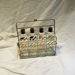May include: A gold metal rack with four clear glass bottles. Each bottle has a black cap and a white and gold striped label. The labels read "Vodka", "Rye", "Bourbon", and "Scotch".