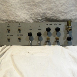 May include: A silver metal panel with various knobs and switches. The panel has labels for "OUT", "RETURN", "cpen", "open", "low cres", "high pres", and "refill".