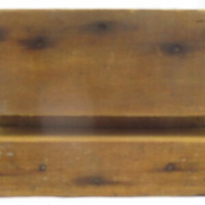 May include: A rectangular wooden block with a horizontal groove running across the center. The wood features a natural light brown tone with visible dark knots and grain patterns throughout the surface, showing a smooth finish on the edges.