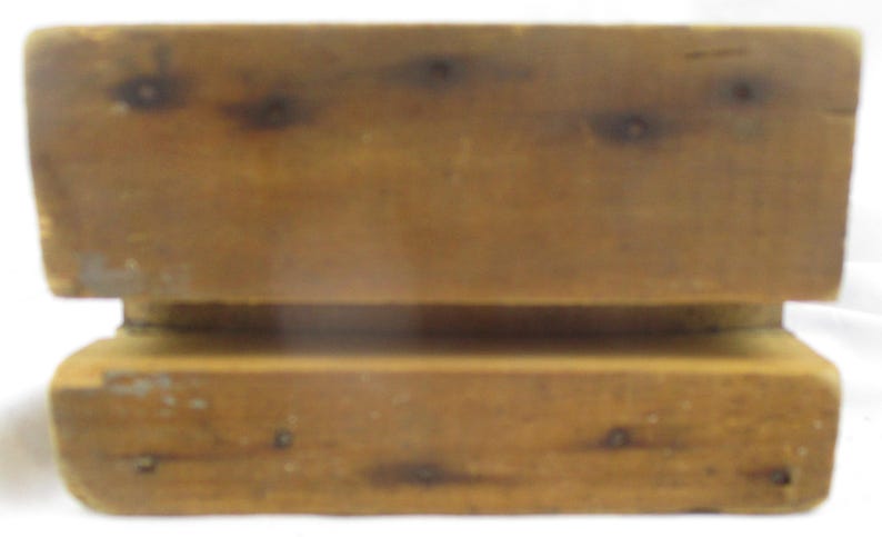 May include: A rectangular wooden block with a horizontal groove running across the center. The wood features a natural light brown tone with visible dark knots and grain patterns throughout the surface, showing a smooth finish on the edges.