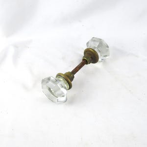 May include: A vintage door knob with two clear, faceted glass knobs. The knobs are connected by a rusty metal rod and brass fittings. The door knob is likely from an antique door.