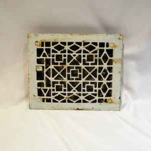 May include: White cast iron floor register with a geometric pattern. The register has a white painted finish with some rust showing through.