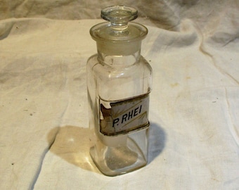 May include: A clear glass bottle with a glass stopper and a label that reads "P.RHEI".