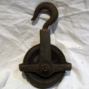 May include: A vintage cast iron pulley with a hook and a wheel with a groove for rope. The pulley is marked "CAPA" on the side.