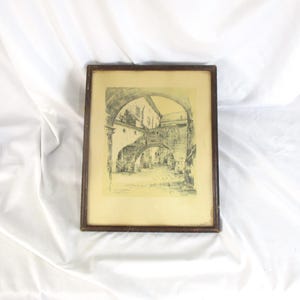 May include: A framed black and white architectural print. The artwork depicts a series of archways and buildings, creating a sense of depth. The frame is a dark brown color, and the print is set against a light background.