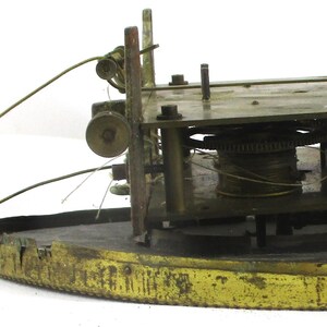 Peut inclure: Un mouvement d'horloge ancien avec des engrenages, des leviers et une base circulaire en laiton. Le m&eacute;canisme est expos&eacute;, r&eacute;v&eacute;lant les composants internes complexes. La base pr&eacute;sente un aspect us&eacute;.