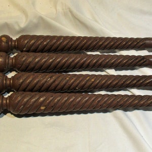 May include: Four dark brown wooden table legs with a twisted design. Each leg has a square base and a rounded top.