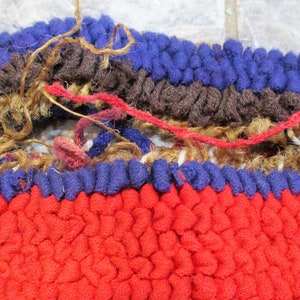 May include: Close-up of a red, blue, and brown woven rug with a hole in the center. The rug is made of thick, looped yarn and has a frayed edge.