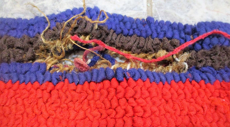 May include: Close-up of a red, blue, and brown woven rug with a hole in the center. The rug is made of thick, looped yarn and has a frayed edge.