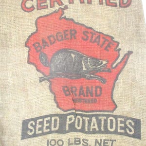 May include: A white ceramic mug with a black handle and the text "But First, Coffee" in a bold, black font. The mug is set against a blurred background, suggesting a cozy setting.