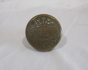 May include: A round, brass door knob with an intricate design of stylized flowers and leaves. The knob has a dark patina and is slightly tarnished.