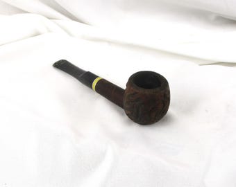 May include: A brown tobacco pipe with a dark mouthpiece and a carved bowl. The pipe has a dark brown stem with a gold-colored band near the bowl. The bowl has a textured, carved design.