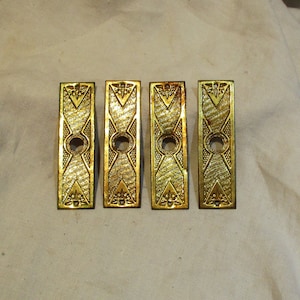 May include: Four antique brass door plates with a decorative geometric design and a keyhole in the center.