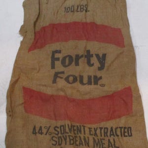 May include: A brown burlap sack with red stripes and the text "Forty Four" and "44% Solvent Extracted Soybean Meal" printed on it. The sack is labeled "100 LBS."