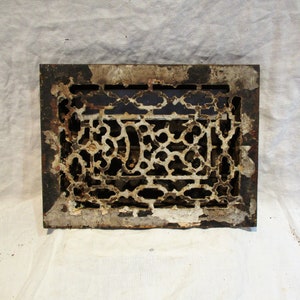 May include: A vintage cast iron floor register with a decorative, intricate design. The register is painted white with some areas showing the original black paint.