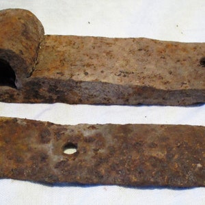 May include: Two rusty metal hinges with a rounded end and a hole in the center. The hinges are made of a dark brown metal and have a rough texture.