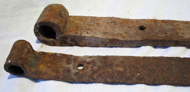 May include: Two rusty metal hinges with a rounded end and a hole in the center. The hinges are made of a dark brown metal and have a rough texture.