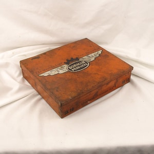 May include: A vintage orange metal box with a white logo that says "Dorman Products" and a winged design. The box has a worn, aged look.