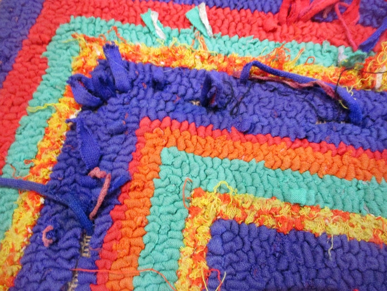 May include: Close-up of a colorful, multi-striped rug with a textured surface. The rug is made of woven fabric and has a frayed edge.