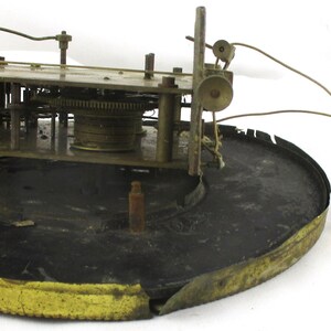 Peut inclure: Un mouvement d'horloge ancien avec des engrenages et des composants en laiton. Le m&eacute;canisme est mont&eacute; sur une base circulaire noire avec un bord dor&eacute;. Des fils et un pendule sont attach&eacute;s.