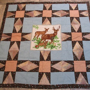 May include: A blue and brown patchwork quilt with a central panel featuring a family of deer. The quilt is made with a variety of fabrics and has a rustic, country feel.