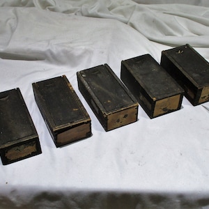May include: Five small wooden boxes with lids, all closed. The boxes are dark brown and have a worn, antique look. Each box has a label on the front, but the text is too blurry to read.