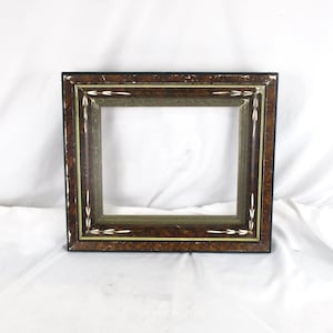 May include: A rectangular picture frame with a dark brown, textured finish. The frame has a black outer edge, a gold inner edge, and white arrow-like accents. The frame is empty, with a visible opening.