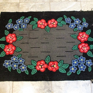 May include: A black rug with a gray center and a floral border. The flowers are red, blue, and green.